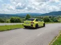Żółte BMW M2 z czterema końcówkami wydechu, czyli otwór pod M4, na tle malowniczych gór i chmur.