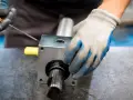 Ręce w rękawiczkach montują element mechaniczny, prawdopodobnie sprzęgła zębate, używając narzędzi.
