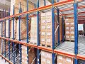 Magazyn z kartonami na regałach typu flow rack. Towary przesuwają się po rolkach, ułatwiając kompletację.
