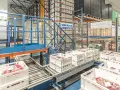 Automatyczny magazyn mięsa, gdzie białe skrzynki z produktami przemieszczają się po taśmociągu, zgodnie z zasadą FEFO.