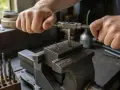 Precyzyjne gwintowanie otworów w metalowym bloku, mocno osadzonym w imadle. Wióry metalu świadczą o pracy narzędzia.