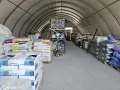 Wnętrze hali magazynowej, gdzie znajduje się strefa składowania wypełniona workami z produktami. Widać regały z towarem i wózek widłowy w tle.