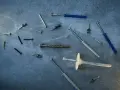 Różne wkręty i kołki rozporowe, w tym jeden z wyraźnym gwintem walcowym, leżą na szarej powierzchni.