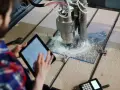Operator nadzoruje obsługę maszyn CNC, kontrolując proces na tablecie. Frezarka precyzyjnie obrabia materiał.