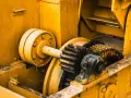 Żółta maszyna z zębatkami, gdzie różne rodzaje smarów chronią mechanizm przed zużyciem.