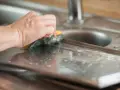 Dłoń czyści metalową powierzchnię gąbką. Dowiedz się, czym wyczyścić aluminium, aby lśniło jak nowe.