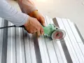 Ręce trzymają szlifierkę kątową, którą tnie się blachę aluminiową wzdłuż czerwonej linii.