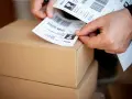 Ręce przygotowują etykiety z kodami kreskowymi do wysyłki. Automatyczna identyfikacja danych ułatwia proces.