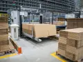 Automatyczna linia pakująca w centrum logistycznym. Stosy kartonów czekają na wypełnienie.
