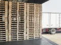 Wysokie stosy drewnianych palet czekają na załadunek. Obok stoi biała ciężarówka, gotowa do transportu. Maksymalna wysokość palety z ładunkiem jest kluczowa dla bezpiecznego przewozu.
