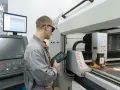 Operator CNC w okularach ochronnych steruje maszyną laserową, która precyzyjnie tnie metal.