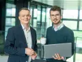 Dwóch mężczyzn w biurze, jeden z laptopem, drugi z kawą. Pracują nad projektem w systemie Symfonia.