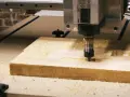 Precyzyjne frezowanie rowków w drewnie za pomocą maszyny CNC. Wióry unoszą się wokół pracującego narzędzia.