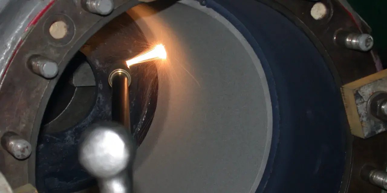 Proces metalizacji natryskowej w toku. Dysza aplikuje materiał na wewnętrzną powierzchnię cylindra, tworząc nową warstwę ochronną.
