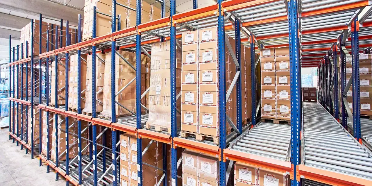 Magazyn z kartonami na regałach typu flow rack. Towary przesuwają się po rolkach, ułatwiając kompletację.