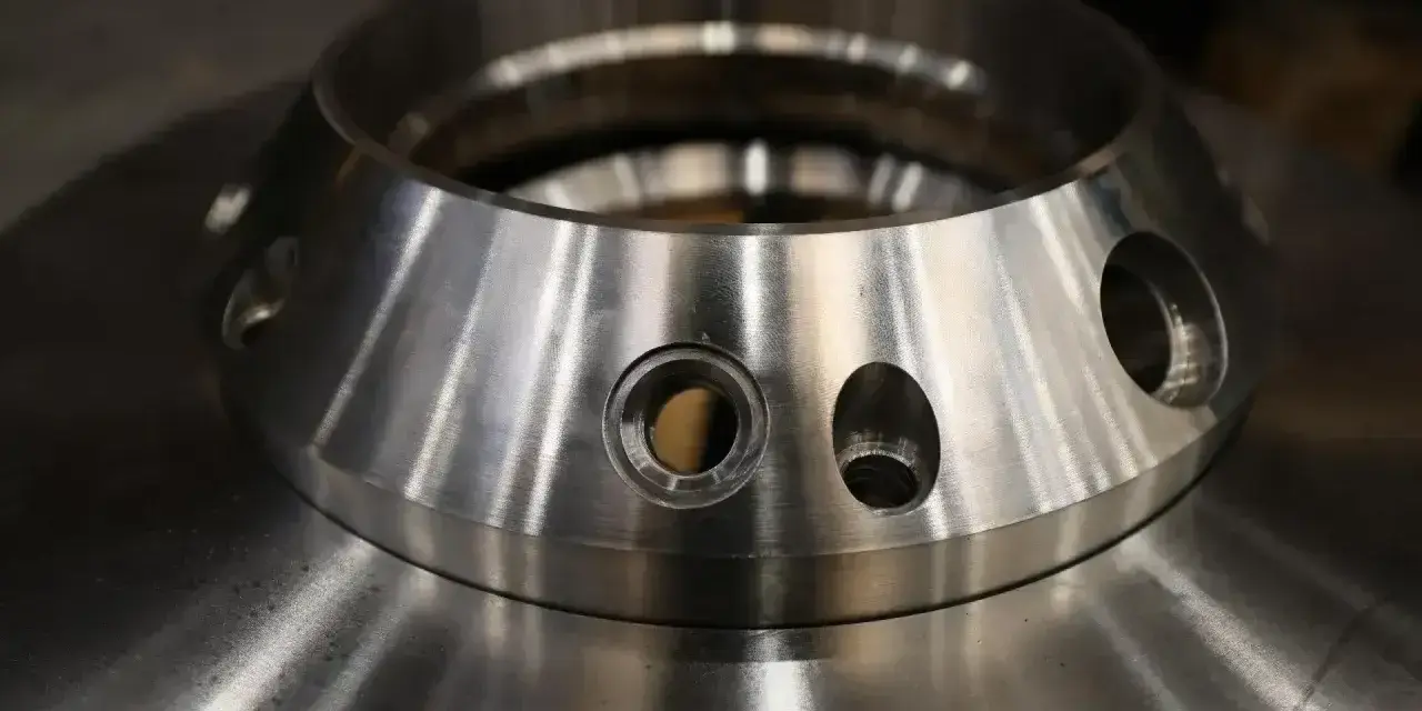 Metalowy element z otworami, przypominający kołnierz. To przykład precyzyjnej obróbki, która może być częścią procesu napawania.