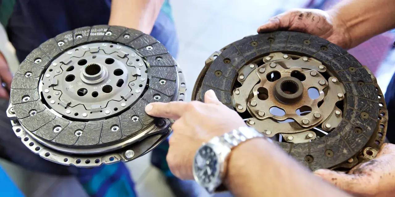 Dwie tarcze sprzęgła, jedna nowa, druga zużyta, prezentowane przez mechanika. Widać mechanizm sprzęgła samonastawne.