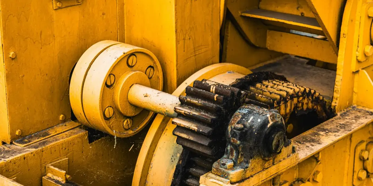 Żółta maszyna z zębatkami, gdzie różne rodzaje smarów chronią mechanizm przed zużyciem.