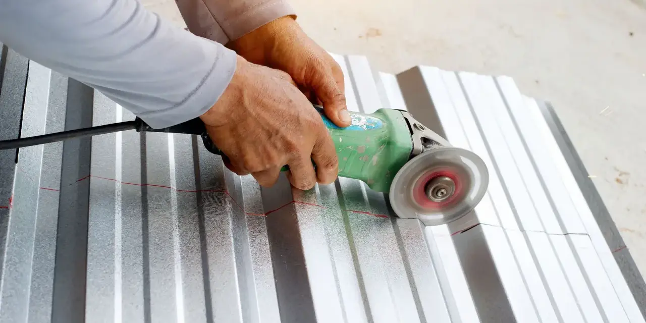 Ręce trzymają szlifierkę kątową, którą tnie się blachę aluminiową wzdłuż czerwonej linii.