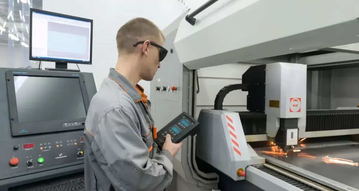 Operator CNC w okularach ochronnych steruje maszyną laserową, która precyzyjnie tnie metal.