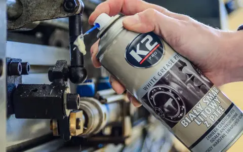 Ręka aplikuje biały smar litowy z PTFE na ruchome części mechanizmu. Idealne biały smar zastosowanie do smarowania i ochrony.