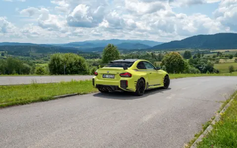 Żółte BMW M2 z czterema końcówkami wydechu, czyli otwór pod M4, na tle malowniczych gór i chmur.