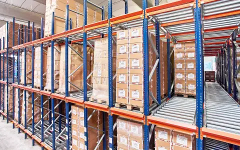 Magazyn z kartonami na regałach typu flow rack. Towary przesuwają się po rolkach, ułatwiając kompletację.