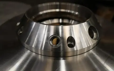 Metalowy element z otworami, przypominający kołnierz. To przykład precyzyjnej obróbki, która może być częścią procesu napawania.