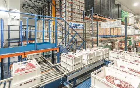 Automatyczny magazyn mięsa, gdzie białe skrzynki z produktami przemieszczają się po taśmociągu, zgodnie z zasadą FEFO.