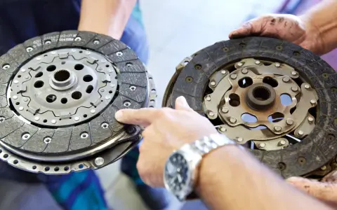 Dwie tarcze sprzęgła, jedna nowa, druga zużyta, prezentowane przez mechanika. Widać mechanizm sprzęgła samonastawne.
