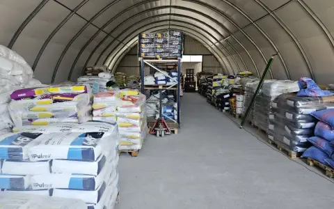 Wnętrze hali magazynowej, gdzie znajduje się strefa składowania wypełniona workami z produktami. Widać regały z towarem i wózek widłowy w tle.
