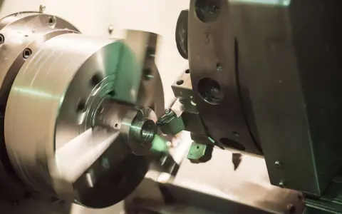 Precyzyjne toczenie aluminium na obrabiarce CNC. Metalowy element obraca się, a narzędzie nadaje mu kształt.