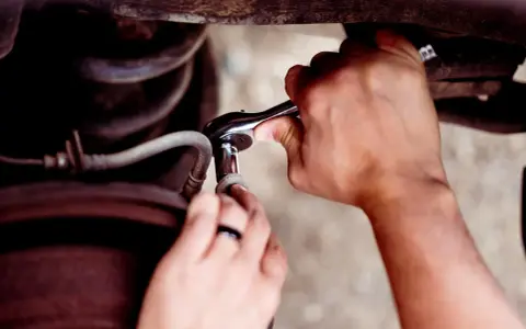 Ręce mechanika używają klucza nasadowego, aby odkręcić śrubę. To pokazuje, jak rozwiercić śrubę w trudnodostępnym miejscu.