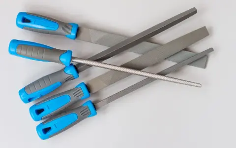 Różne rodzaje pilników do metalu: płaskie, okrągłe i trójkątne, z niebiesko-szarymi rękojeściami.