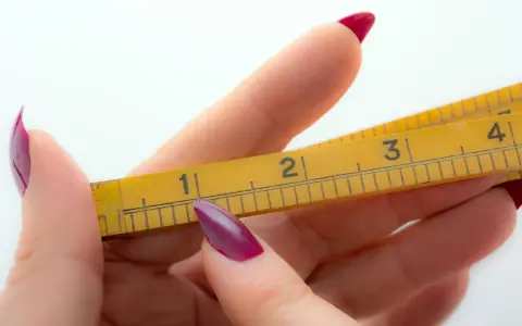 Dłoń z bordowymi paznokciami trzyma żółtą miarkę. Widoczne są oznaczenia 1, 2, 3, 4. Zastanawiasz się, ile to mm, gdy gwint 1 cal?