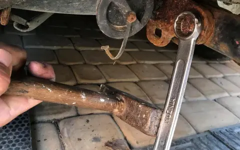 Próba odkręcenia zapieczonej śruby młotkiem i kluczem. Rdza i trudności w demontażu.