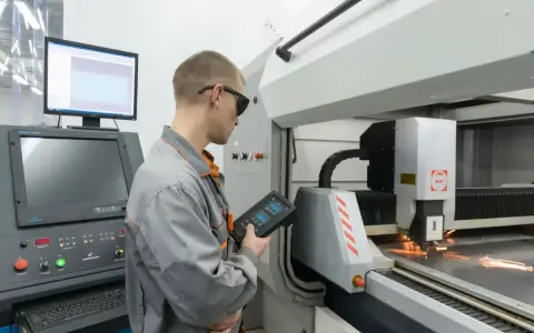 Operator CNC w okularach ochronnych steruje maszyną laserową, która precyzyjnie tnie metal.