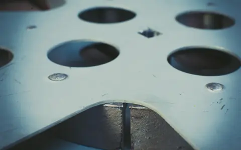 Metalowa płyta z wieloma okrągłymi otworami, widoczne ślady po rozwiercaniu.