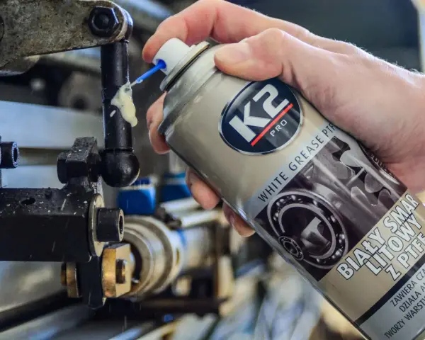 Ręka aplikuje biały smar litowy z PTFE na ruchome części mechanizmu. Idealne biały smar zastosowanie do smarowania i ochrony.