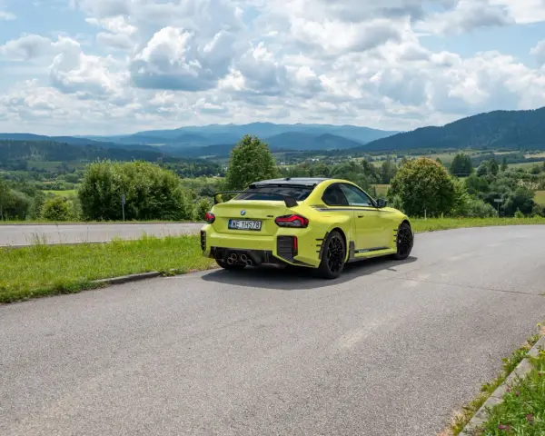 Żółte BMW M2 z czterema końcówkami wydechu, czyli otwór pod M4, na tle malowniczych gór i chmur.