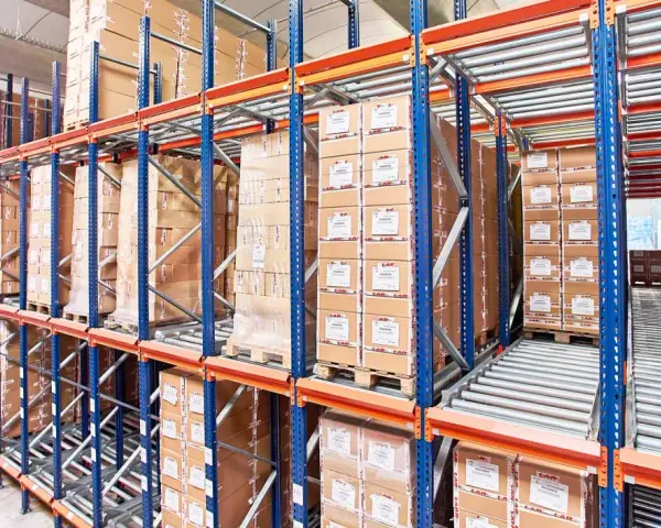 Magazyn z kartonami na regałach typu flow rack. Towary przesuwają się po rolkach, ułatwiając kompletację.