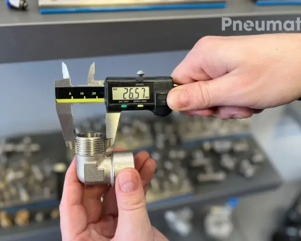 Precyzyjne pomiary gwintów zewnętrznych kolanka pneumatycznego suwmiarką cyfrową. Wynik 26.57 mm.