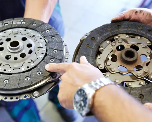 Dwie tarcze sprzęgła, jedna nowa, druga zużyta, prezentowane przez mechanika. Widać mechanizm sprzęgła samonastawne.