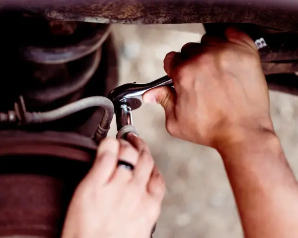 Ręce mechanika używają klucza nasadowego, aby odkręcić śrubę. To pokazuje, jak rozwiercić śrubę w trudnodostępnym miejscu.