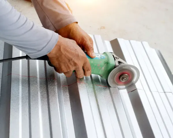 Ręce trzymają szlifierkę kątową, którą tnie się blachę aluminiową wzdłuż czerwonej linii.