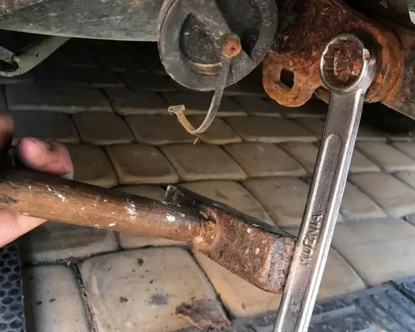 Próba odkręcenia zapieczonej śruby młotkiem i kluczem. Rdza i trudności w demontażu.