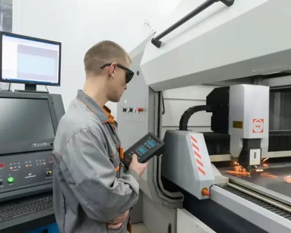 Operator CNC w okularach ochronnych steruje maszyną laserową, która precyzyjnie tnie metal.