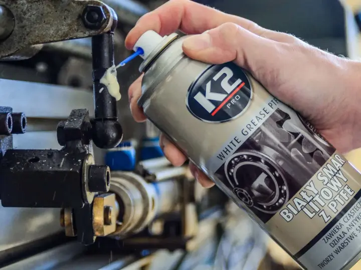 Ręka aplikuje biały smar litowy z PTFE na ruchome części mechanizmu. Idealne biały smar zastosowanie do smarowania i ochrony.