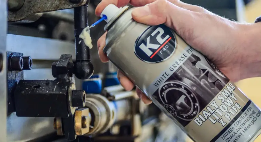Ręka aplikuje biały smar litowy z PTFE na ruchome części mechanizmu. Idealne biały smar zastosowanie do smarowania i ochrony.