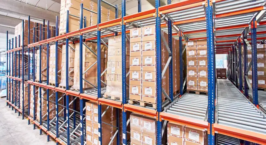 Magazyn z kartonami na regałach typu flow rack. Towary przesuwają się po rolkach, ułatwiając kompletację.